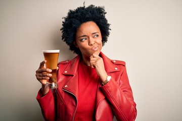 Young African American afro woman with curly hair drinking glass of beer with alcohol serious face...