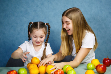 Fototapeta premium Little girl and mom play with fruits and fool around. They are wearing t-shirts