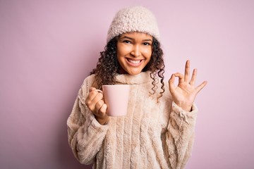 Young beautiful woman with curly hair drinking mug of coffee over isolated pink background doing ok sign with fingers, excellent symbol