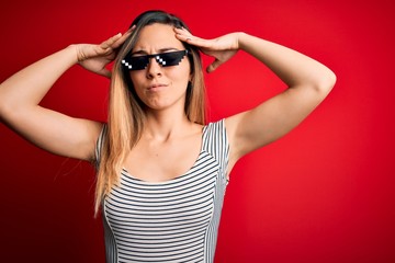 Young beautiful brunette woman wearing funny thug life sunglasses over red background suffering from headache desperate and stressed because pain and migraine. Hands on head.