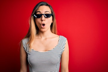 Naklejka premium Young beautiful brunette woman wearing funny thug life sunglasses over red background afraid and shocked with surprise expression, fear and excited face.