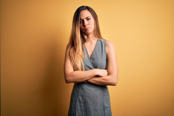 Obraz premium Young beautiful blonde woman with blue eyes wearing dress over yellow background skeptic and nervous, disapproving expression on face with crossed arms. Negative person.