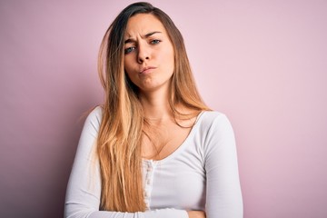 Young beautiful blonde woman with blue eyes wearing white t-shirt over pink background skeptic and...
