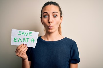 Young beautiful woman holding paper asking for save earth and enviroment conservation scared in shock with a surprise face, afraid and excited with fear expression