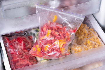 Plastic bags with different frozen vegetables in refrigerator, frozen pepper