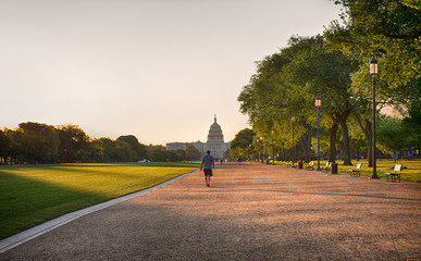 A man dressed in T shirt, shorts and cap taking a brisk walk, away from the camera, through the...