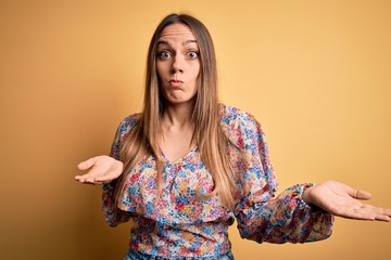 Young beautiful blonde woman with blue eyes wearing summer clothes over yellow background clueless and confused expression with arms and hands raised. Doubt concept.