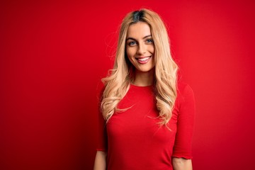 Fototapeta premium Young beautiful blonde woman wearing casual t-shirt standing over isolated red background with a happy and cool smile on face. Lucky person.