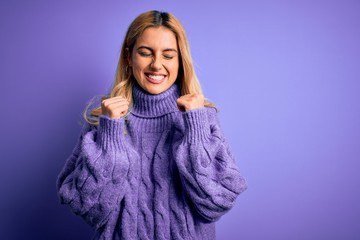 Young beautiful blonde woman wearing casual turtleneck sweater over purple background excited for success with arms raised and eyes closed celebrating victory smiling. Winner concept.