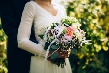 Wedding bouquet composed of roses,other types of flowers,decorative leaves and completed with white ribbon with lace.Bride holding bouquet in hands of groom's victim.Image with shallow depth of field.