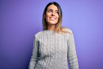 Young beautiful woman wearing casual sweater standing over isolated purple background looking away to side with smile on face, natural expression. Laughing confident.