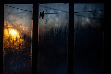 Sunrise outside the window. Misted glass against the backdrop of the rising sun. Winter morning. . Simple background. The ratio of cold and warm colors. Texture of water condensate on glass.