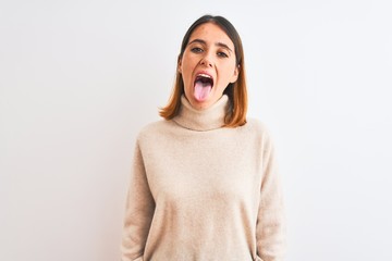 Beautiful redhead woman wearing winter turtleneck sweater over isolated background sticking tongue...