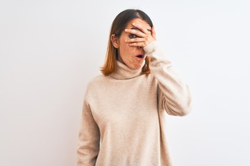 Beautiful redhead woman wearing winter turtleneck sweater over isolated background peeking in shock covering face and eyes with hand, looking through fingers with embarrassed expression.