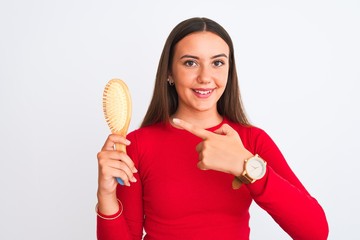 Young beautiful girl holding hair comb standing over isolated white background very happy pointing with hand and finger