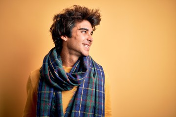 Young handsome man wearing casual scarf standing over isolated yellow background looking away to side with smile on face, natural expression. Laughing confident.