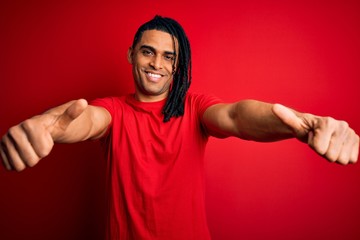 Naklejka premium Young handsome african american afro man with dreadlocks wearing red casual t-shirt approving doing positive gesture with hand, thumbs up smiling and happy for success. Winner gesture.