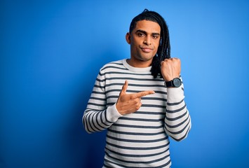 Fototapeta premium Young handsome african american afro man with dreadlocks wearing casual striped sweater In hurry pointing to watch time, impatience, looking at the camera with relaxed expression