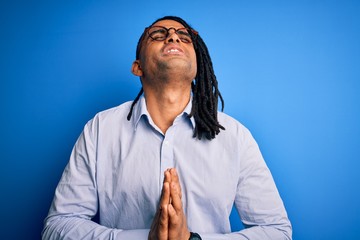 Young handsome african american man with dreadlocks wearing casual shirt and glasses begging and praying with hands together with hope expression on face very emotional and worried. Begging.