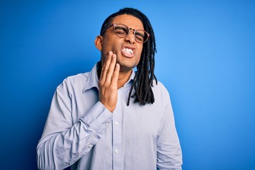 Young handsome african american man with dreadlocks wearing casual shirt and glasses touching mouth with hand with painful expression because of toothache or dental illness on teeth. Dentist