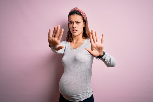 Young beautiful teenager girl pregnant expecting baby over isolated pink background doing stop gesture with hands palms, angry and frustration expression