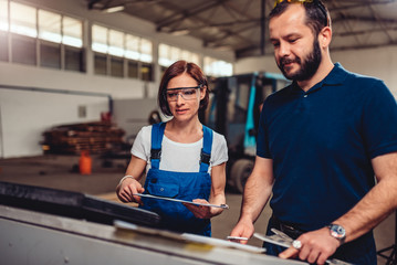 Female CNC machine operator checking program code with supervisor