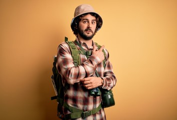 Young hiker man with curly hair and beard hiking wearing backpack and water canteen Pointing aside...