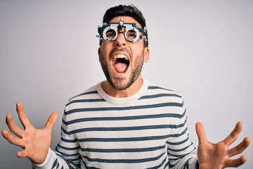 Fototapeta premium Young handsome man with beard wearing optometry glasses over isolated white background crazy and mad shouting and yelling with aggressive expression and arms raised. Frustration concept.