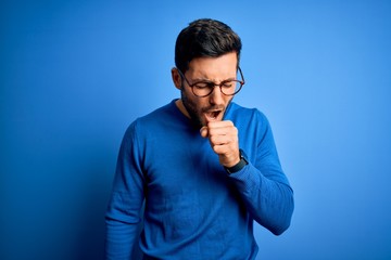 Young handsome man with beard wearing casual sweater and glasses over blue background feeling unwell and coughing as symptom for cold or bronchitis. Health care concept.