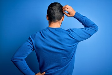 Young handsome man with beard wearing casual sweater and glasses over blue background Backwards thinking about doubt with hand on head