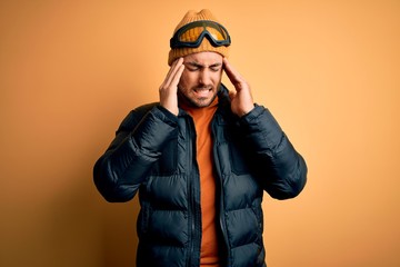 Young handsome skier man with beard wearing snow sportswear and ski goggles with hand on headache because stress. Suffering migraine.