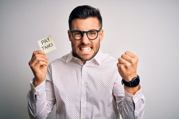 Young handsome man holding reminder paper with pay taxes message over white background annoyed and...