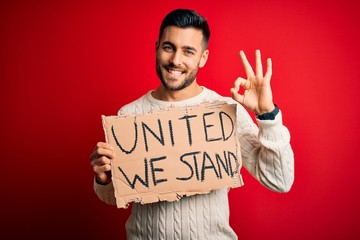 Young handsome activist man protesting holding cardboard with unity message doing ok sign with...