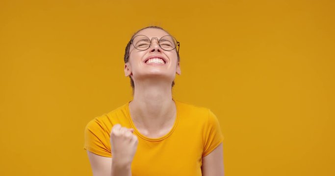 Young pretty fan girl shouting while her team wins, raised fist in victory gesture, isolated on studio yellow background