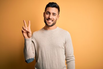 Young handsome man wearing casual sweater standing over isolated yellow background smiling with...
