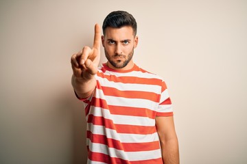 Fototapeta premium Young handsome man wearing casual striped t-shirt standing over isolated white background Pointing with finger up and angry expression, showing no gesture