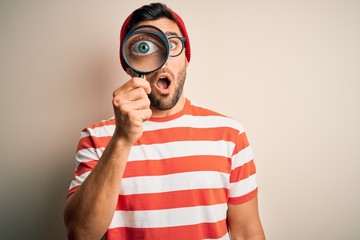 Young detective man looking through magnifying glass over isolated background scared in shock with a surprise face, afraid and excited with fear expression