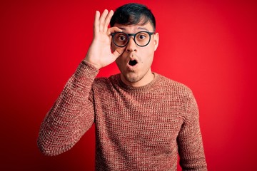 Young handsome hispanic man wearing nerd glasses over red background doing ok gesture shocked with...