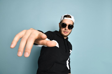 Hipster male in cap, black tracksuit and sunglasses. He is pointing at you by his forefinger,...