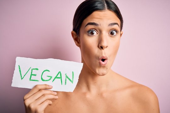 Young beautiful girl holding paper with vegan message over isolated pink background scared in shock with a surprise face, afraid and excited with fear expression
