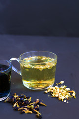 Jasmine tea. Hot drinks. Healthy lifestyle. glass cup of Jasmine tea on a black background. cup of hot herbal tea with dry flowers of Jasmine on a black table. copy space. vertical orientation