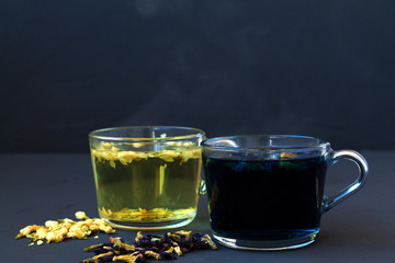 Hot butterfly pea tea and Jasmine tea. Healthy lifestyle. glass cups of blue and yellow herbal tea on a black background. Hot drinks. two cups of hot tea with dry flowers on a black table. copy space.