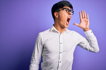 Fototapeta premium Young handsome business man wearing shirt and glasses over isolated purple background shouting and screaming loud to side with hand on mouth. Communication concept.