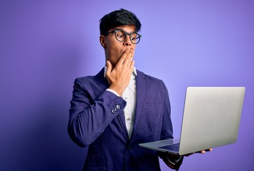 Young handsome business man wearing glasses working using laptop over purple background cover mouth with hand shocked with shame for mistake, expression of fear, scared in silence, secret concept