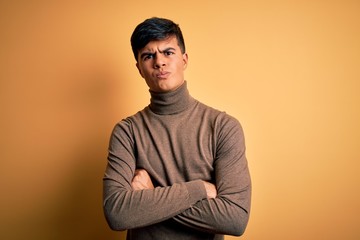 Young handsome man wearing casual turtleneck sweater over isolated yellow background skeptic and nervous, disapproving expression on face with crossed arms. Negative person.