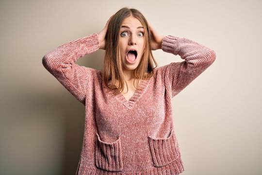 Young beautiful redhead woman wearing pink casual sweater over isolated white background Crazy and scared with hands on head, afraid and surprised of shock with open mouth