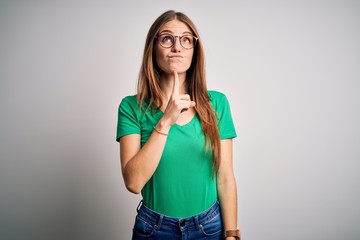 Young beautiful redhead woman wearing casual green t-shirt and glasses over white background...