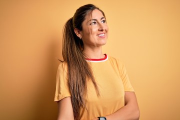 Obraz premium Young beautiful athletic woman wearing casual t-shirt and ponytail over yellow background looking away to side with smile on face, natural expression. Laughing confident.