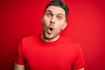 Young man with blue eyes wearing casual t-shirt over red isolated background afraid and shocked with surprise expression, fear and excited face.