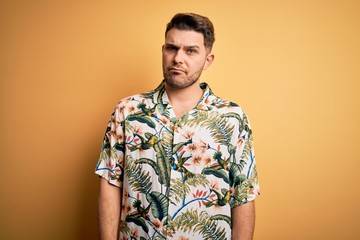 Young man with blue eyes on vacation wearing floral summer shirt over yellow background skeptic and nervous, frowning upset because of problem. Negative person.